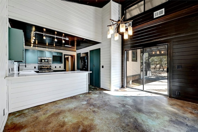 interior space featuring range with electric stovetop, stainless steel microwave, wood walls, a sink, and concrete flooring