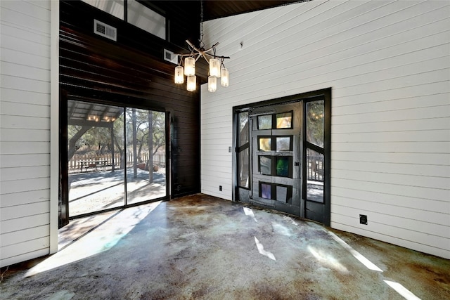 interior space featuring wood walls, concrete floors, visible vents, and an inviting chandelier