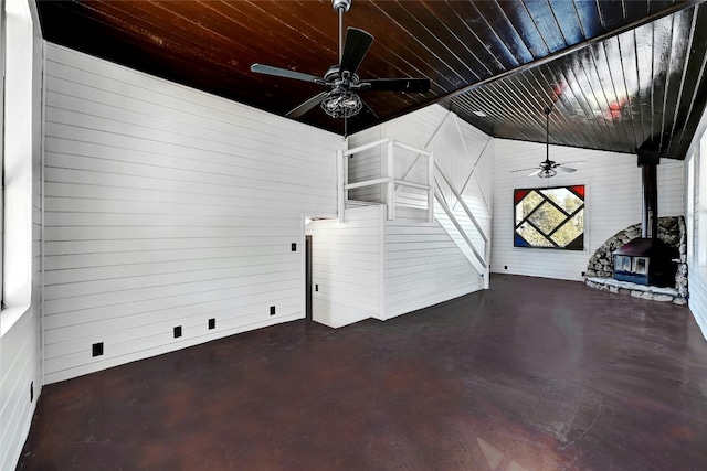 unfurnished living room featuring a wood stove, ceiling fan, wood ceiling, and concrete flooring