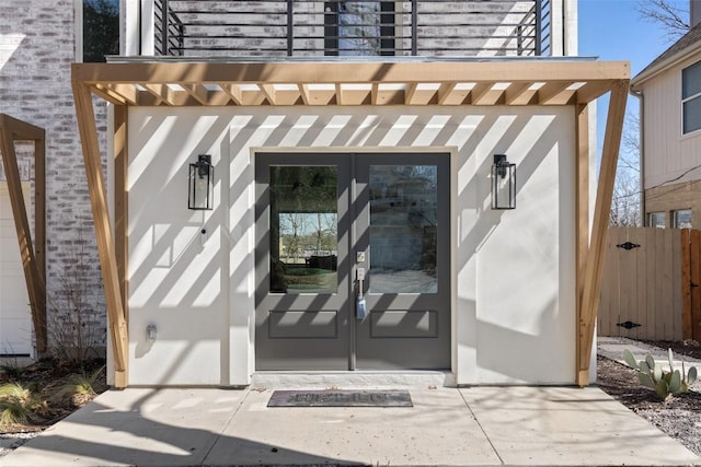 view of exterior entry with french doors, fence, and a pergola