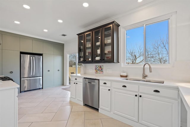 kitchen featuring light countertops, a sink, appliances with stainless steel finishes, glass insert cabinets, and visible vents