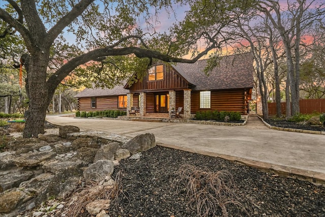 cabin featuring a shingled roof, fence, driveway, log exterior, and board and batten siding