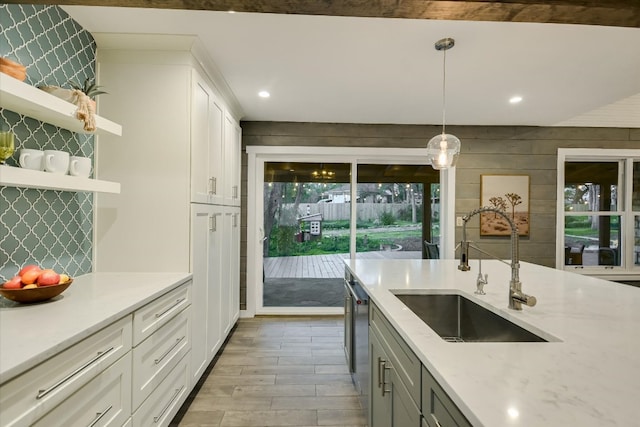 kitchen with light wood-style flooring, a sink, white cabinetry, backsplash, and decorative light fixtures