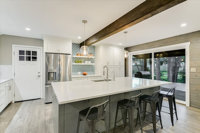 kitchen featuring stainless steel refrigerator with ice dispenser, decorative backsplash, white cabinets, a sink, and beamed ceiling