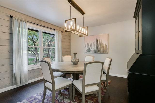 dining space featuring dark wood-style flooring, wood walls, baseboards, and an inviting chandelier