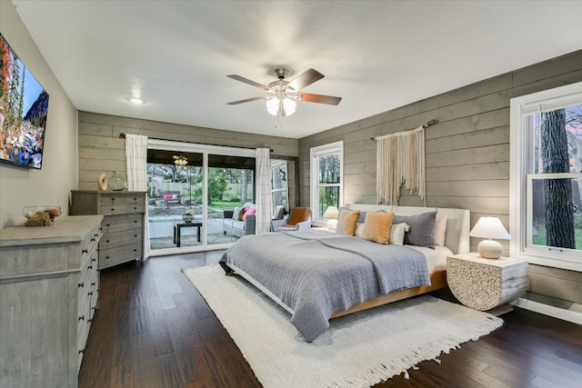 bedroom featuring access to exterior, dark wood-style flooring, a ceiling fan, wood walls, and baseboards