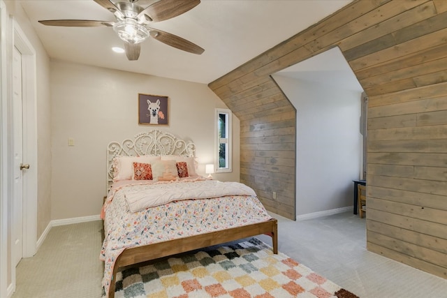 carpeted bedroom featuring vaulted ceiling, wooden walls, baseboards, and ceiling fan