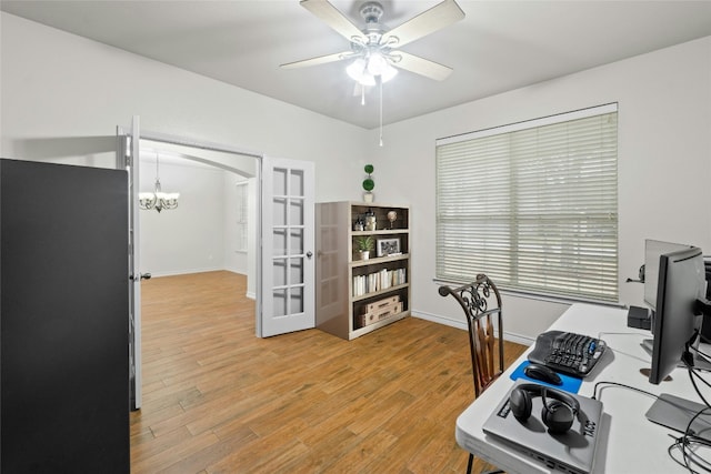 office area featuring baseboards, arched walkways, french doors, light wood-style floors, and ceiling fan with notable chandelier