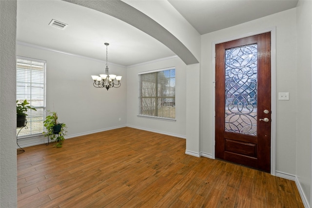 foyer entrance with arched walkways, wood finished floors, visible vents, and baseboards