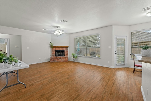 living area featuring ceiling fan, a brick fireplace, wood finished floors, and visible vents