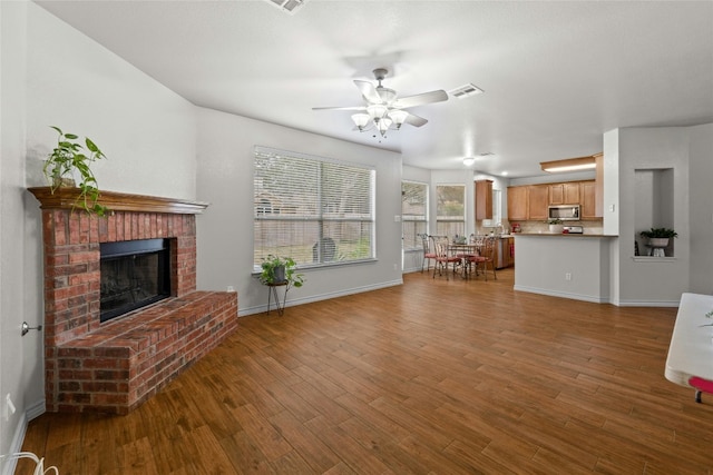 unfurnished living room featuring a fireplace, wood finished floors, a ceiling fan, visible vents, and baseboards