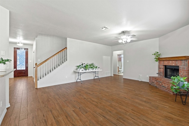 living room with hardwood / wood-style flooring, visible vents, a ceiling fan, stairway, and a brick fireplace