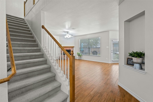 stairs featuring ceiling fan, a fireplace, wood finished floors, visible vents, and baseboards