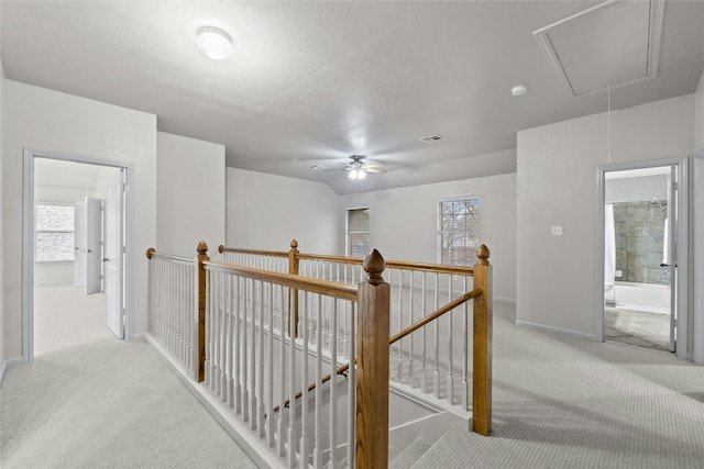 hall with attic access, visible vents, carpet floors, and an upstairs landing