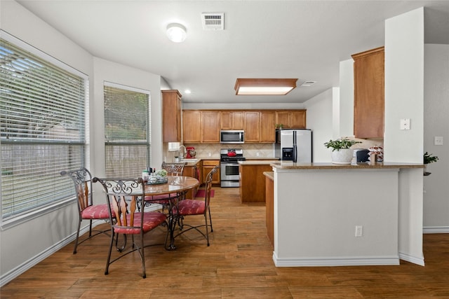 kitchen featuring stainless steel appliances, backsplash, wood finished floors, and brown cabinets