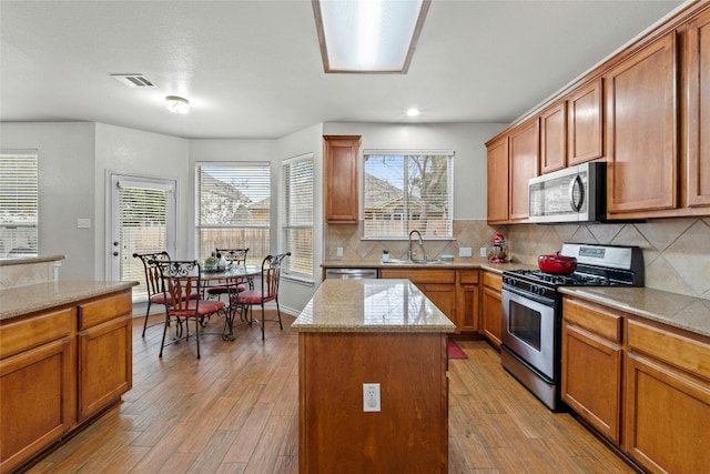 kitchen with stainless steel appliances, a sink, visible vents, light wood-style floors, and backsplash