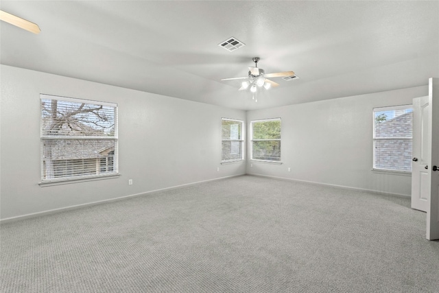 carpeted spare room featuring a healthy amount of sunlight, baseboards, visible vents, and a ceiling fan