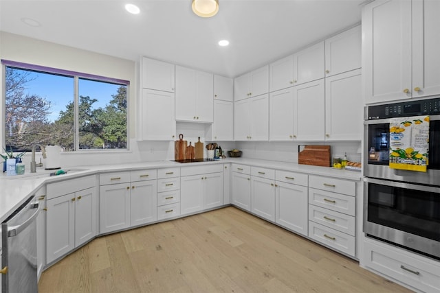 kitchen featuring light wood finished floors, light countertops, appliances with stainless steel finishes, white cabinetry, and a sink