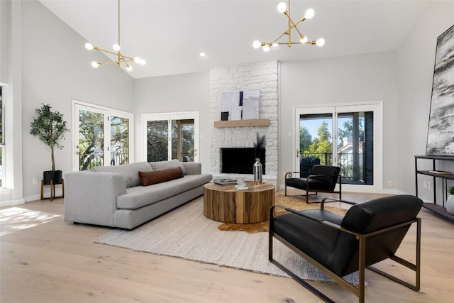 living area featuring a fireplace, a notable chandelier, light wood-style flooring, high vaulted ceiling, and baseboards