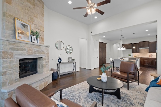 living area with a stone fireplace, dark wood finished floors, a ceiling fan, and recessed lighting