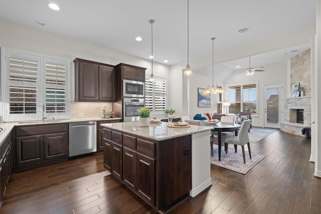 kitchen featuring dark brown cabinetry, open floor plan, stainless steel appliances, a stone fireplace, and a sink