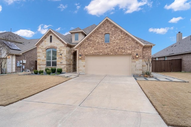 french country home featuring driveway, a shingled roof, stone siding, fence, and brick siding