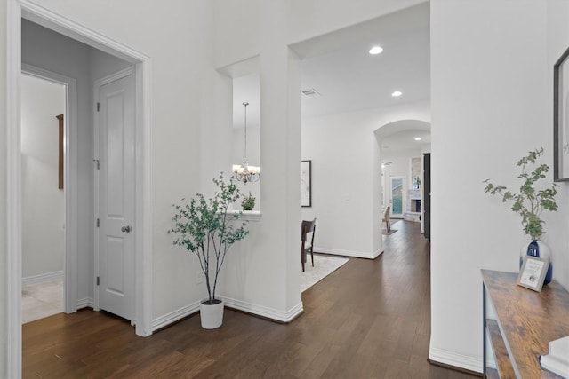 hallway with dark wood-style floors, arched walkways, recessed lighting, an inviting chandelier, and baseboards