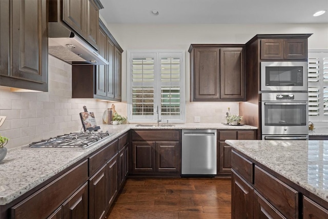 kitchen with stainless steel appliances, dark brown cabinets, dark wood-style flooring, and under cabinet range hood