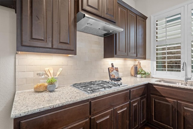 kitchen featuring dark brown cabinetry, under cabinet range hood, stainless steel gas stovetop, and a sink