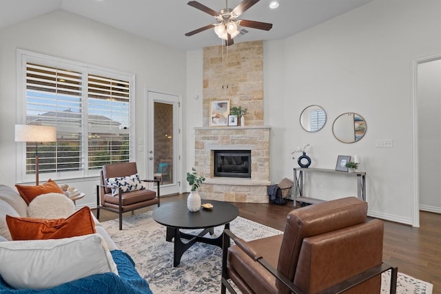 living area with ceiling fan, vaulted ceiling, a stone fireplace, wood finished floors, and baseboards