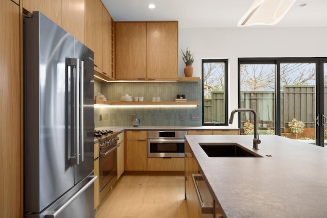 kitchen with premium appliances, light countertops, light wood-style flooring, decorative backsplash, and a sink