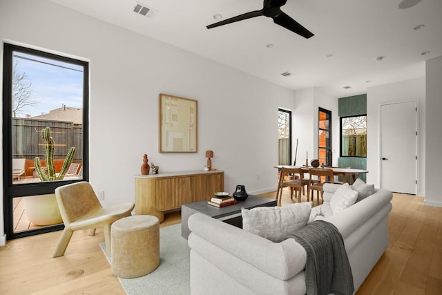 living room featuring baseboards, visible vents, ceiling fan, and light wood finished floors