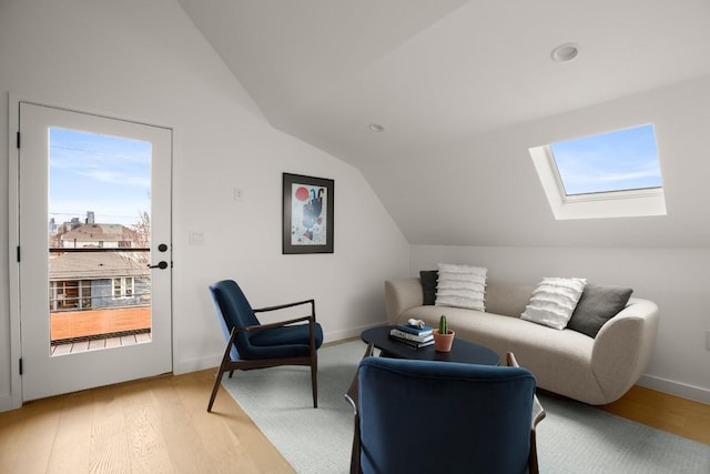 living area featuring vaulted ceiling with skylight, light wood finished floors, and baseboards