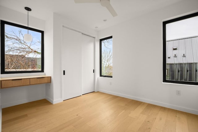 unfurnished bedroom featuring a ceiling fan, a closet, light wood-style flooring, and baseboards