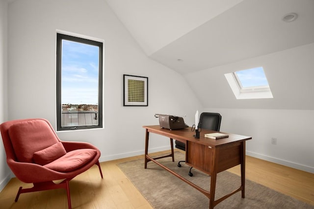 office area with light wood-style floors, vaulted ceiling with skylight, and baseboards