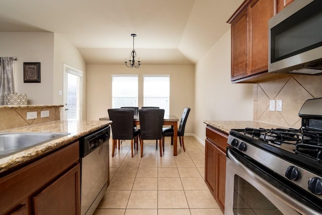 kitchen with light tile patterned floors, stainless steel appliances, vaulted ceiling, decorative backsplash, and brown cabinetry