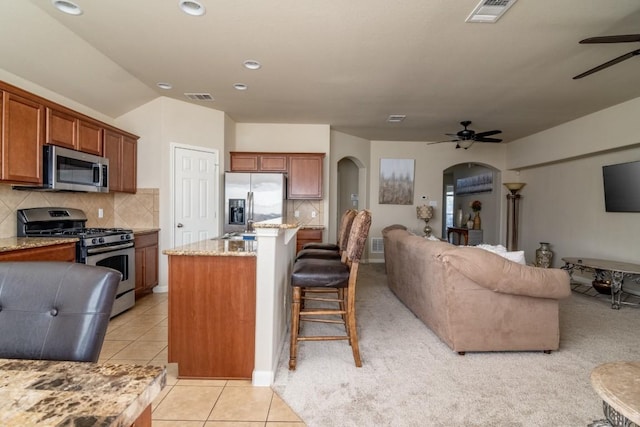 kitchen featuring arched walkways, light tile patterned floors, stainless steel appliances, visible vents, and open floor plan