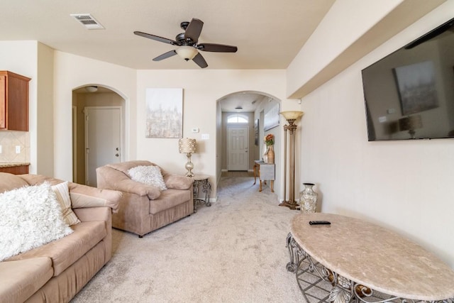 living area featuring light colored carpet, arched walkways, visible vents, and a ceiling fan