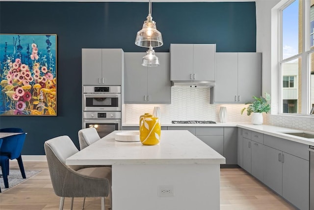 kitchen featuring gas cooktop, under cabinet range hood, a center island, decorative backsplash, and a kitchen bar