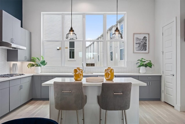 kitchen with light wood-style flooring, a center island, gray cabinets, stainless steel gas stovetop, and backsplash