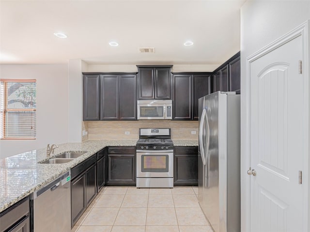 kitchen featuring light tile patterned floors, a sink, appliances with stainless steel finishes, backsplash, and light stone countertops