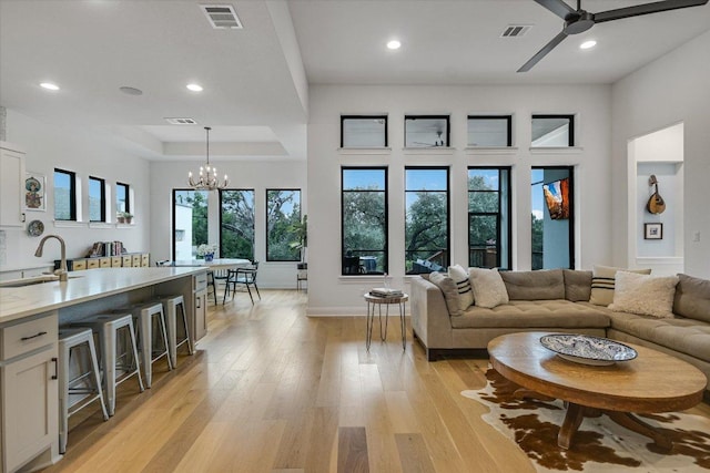 living room featuring light wood-type flooring, recessed lighting, visible vents, and ceiling fan with notable chandelier