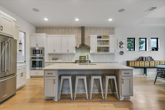 kitchen with stainless steel appliances, a breakfast bar, visible vents, and wall chimney exhaust hood