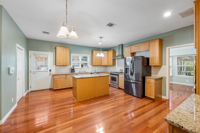 kitchen with visible vents, fridge with ice dispenser, wall chimney range hood, a sink, and gas stove