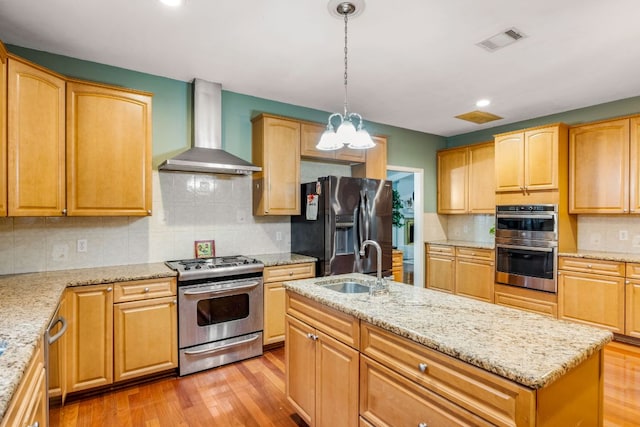 kitchen featuring visible vents, light wood-style flooring, appliances with stainless steel finishes, wall chimney range hood, and a sink