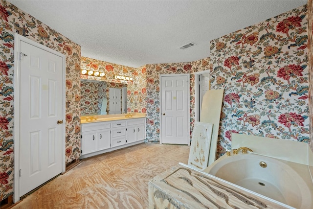 bathroom with a textured ceiling, visible vents, a whirlpool tub, double vanity, and wallpapered walls