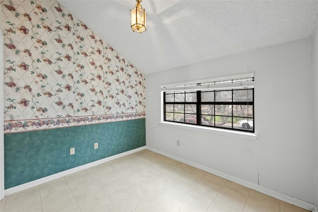 spare room with a textured ceiling, lofted ceiling, an accent wall, baseboards, and wallpapered walls