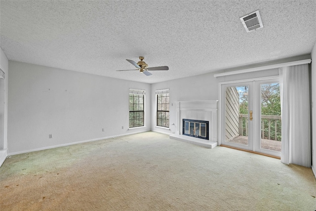 unfurnished living room with ceiling fan, a textured ceiling, visible vents, carpet, and a glass covered fireplace