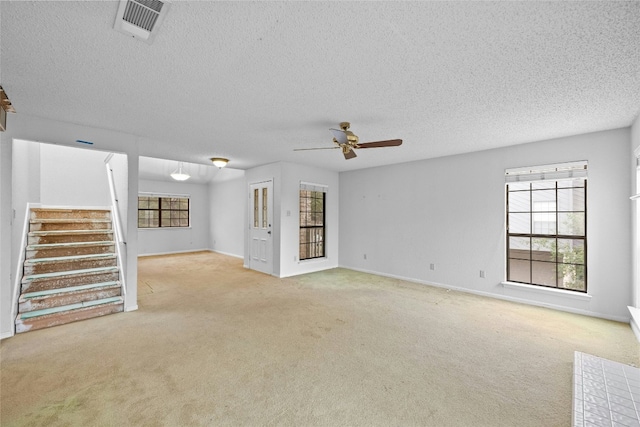 unfurnished living room featuring visible vents, a ceiling fan, stairs, carpet flooring, and a textured ceiling