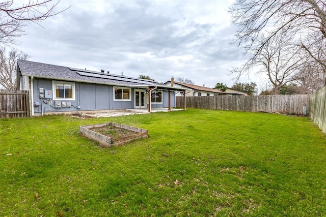 back of property with a garden, a lawn, a patio, a fenced backyard, and roof mounted solar panels